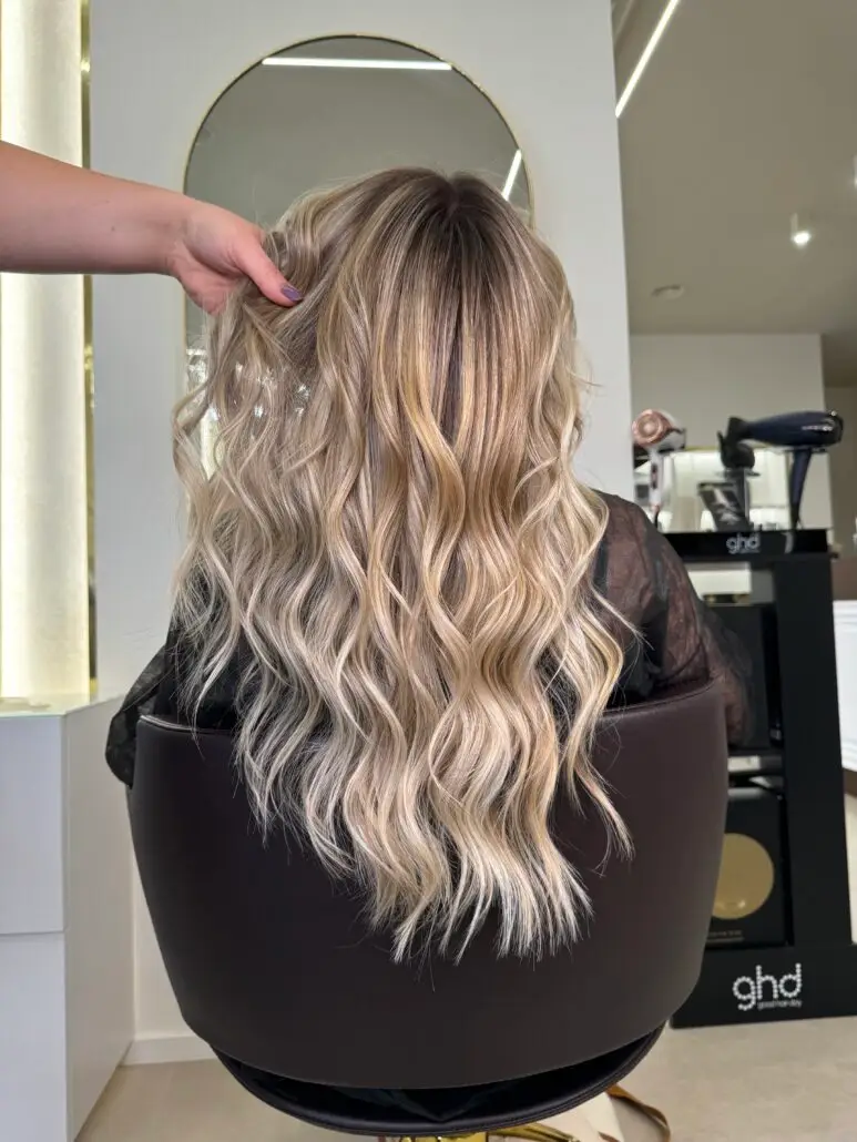 Lunga chioma biondo freddo con schiaritura balayage e onde morbide, realizzata nel BROSS Hair Lounge con il Metodo BROSS™. Styling elegante, rifinito a mano.